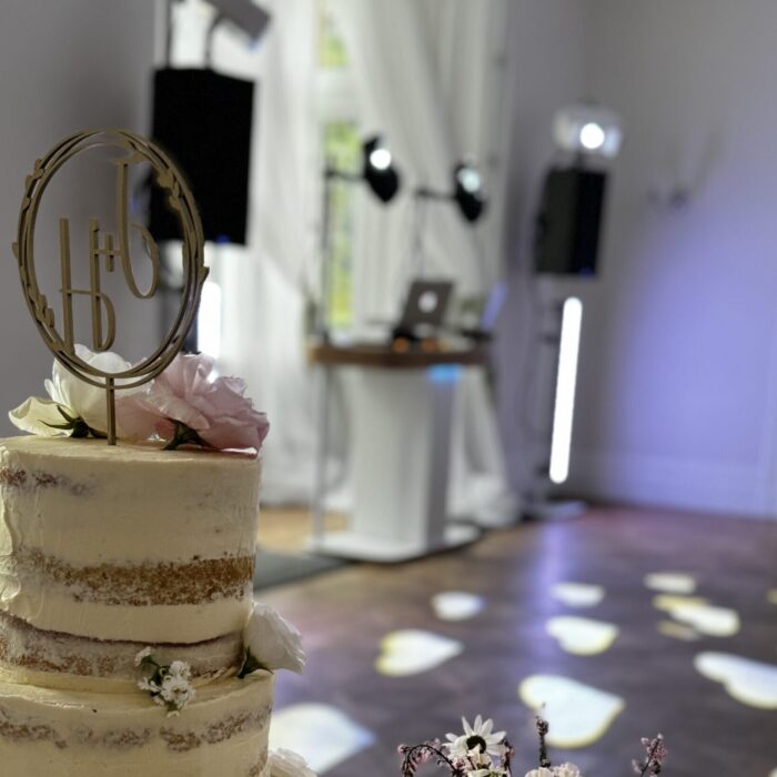 A white shabby chic wedding cake sits in front of a disco show ready to begin the evening's party